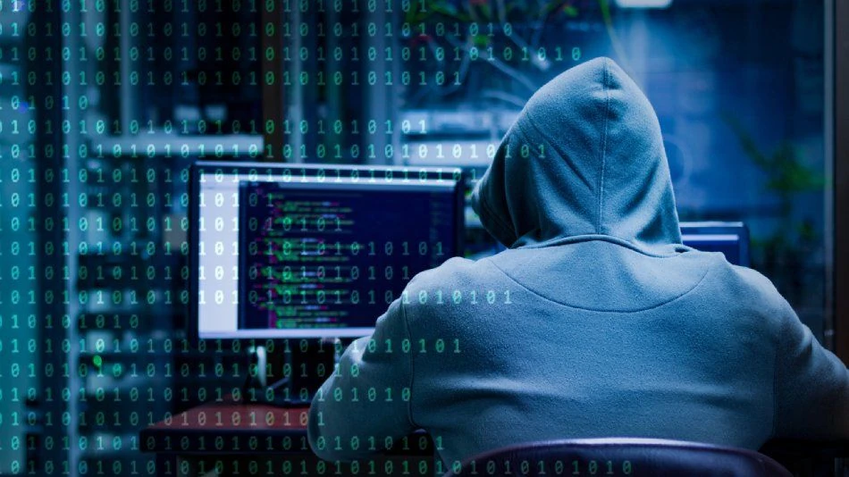 Persona con capucha frente a múltiples pantallas mostrando números binarios, simbolizando a un hacker.